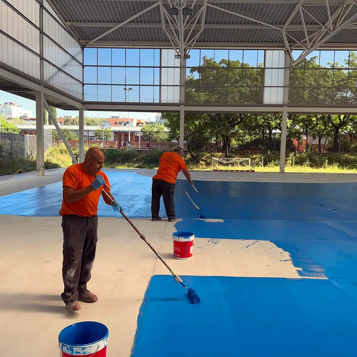 Two applicators rolling the blue coat across the pavilion floor, Granollers