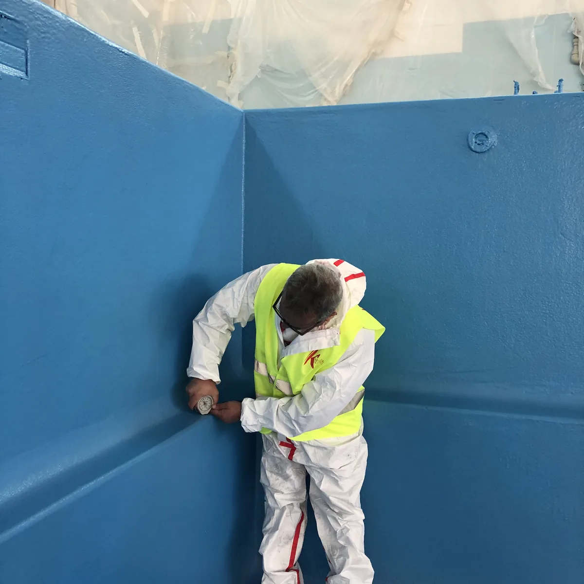 Applicator in hi-vis vest beside a blue-finished pool wall, Nizhny Novgorod