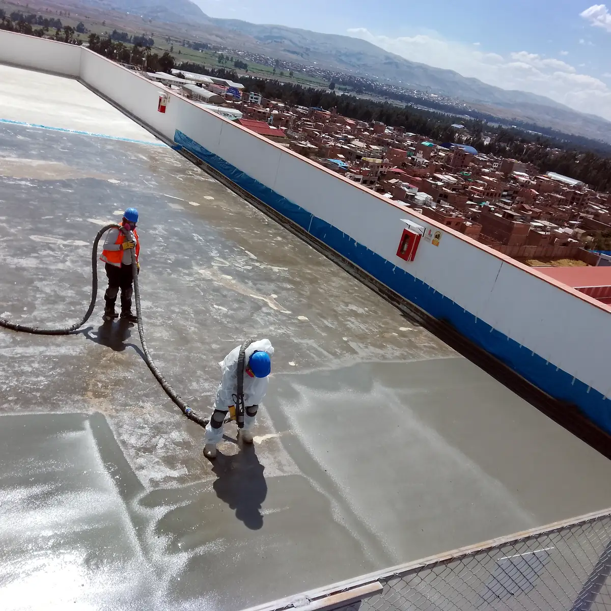 Operarios lavando el soporte preparado de la cubierta con la ciudad al fondo