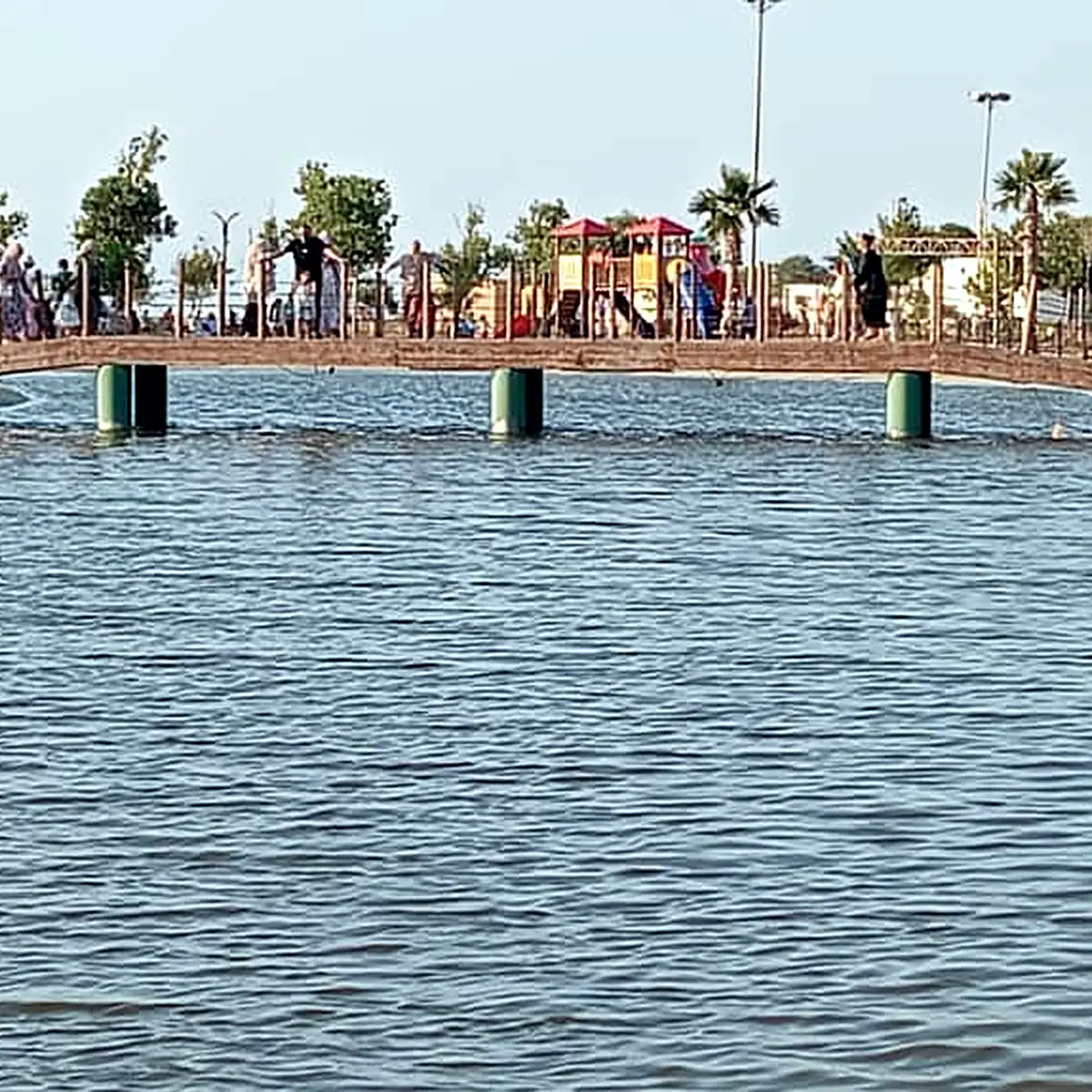 Calm lake water and the footbridge seen from the bank in 2026