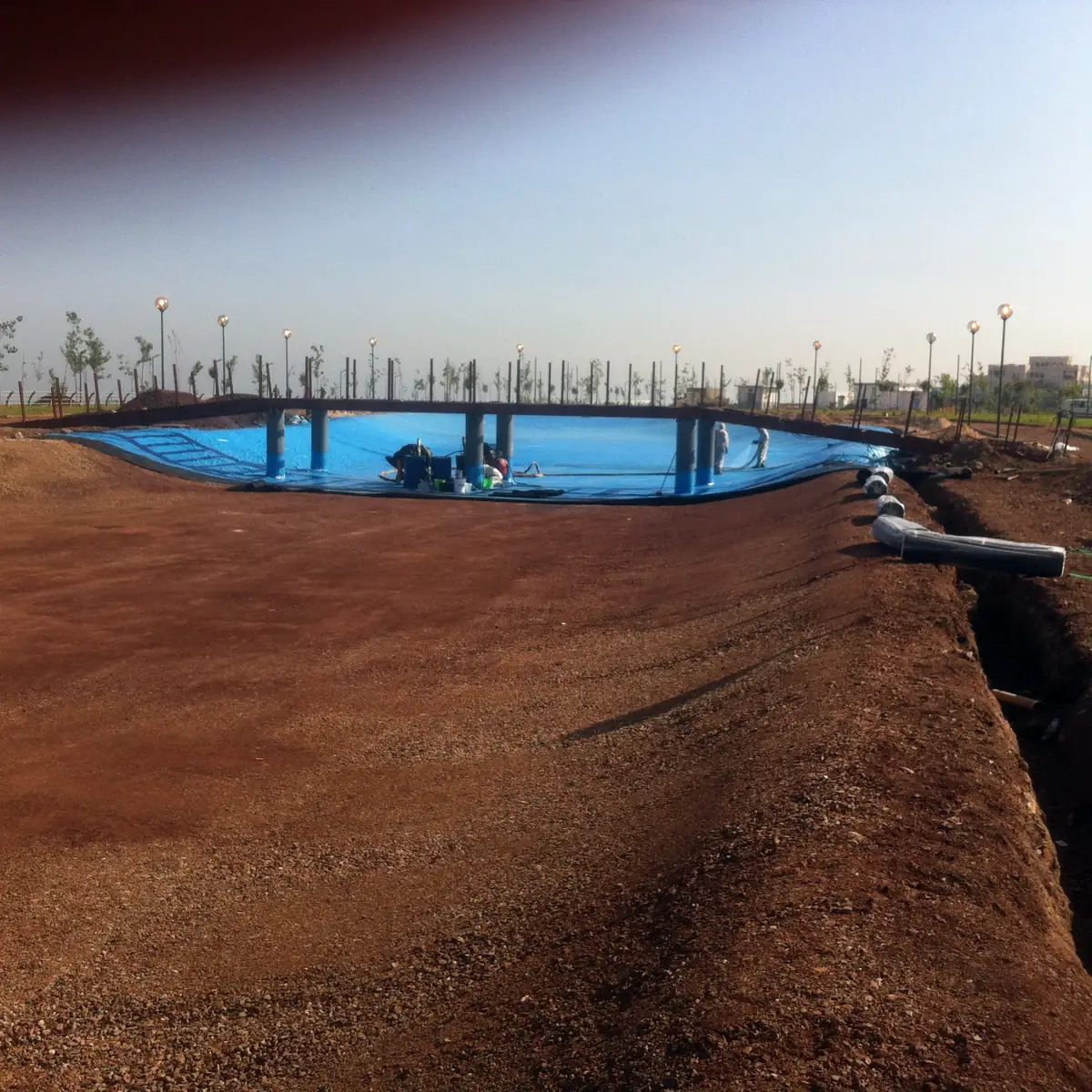 Open trench in the red earth leading toward the lined lake