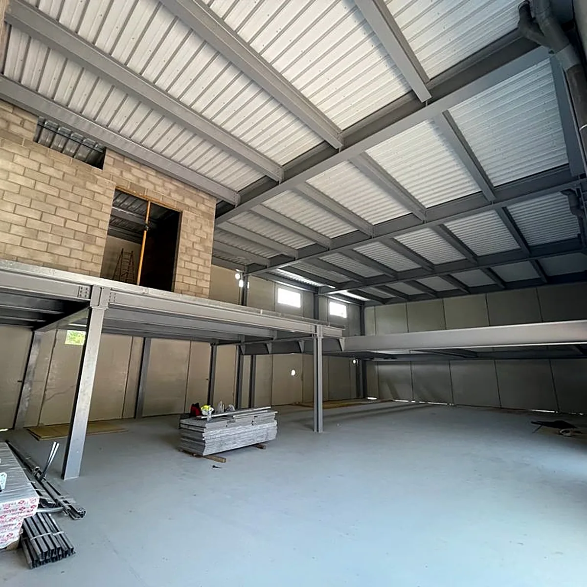 Wide hall with a grey resin floor below a steel mezzanine, Viladrau
