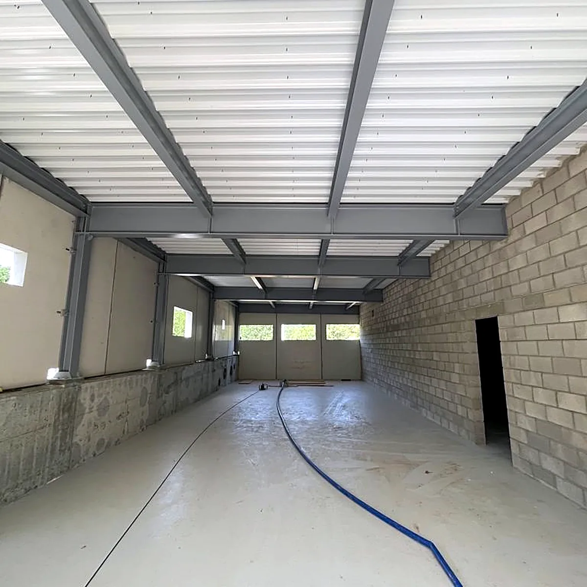 Long machinery hall with a grey epoxy floor and a block wall, Viladrau