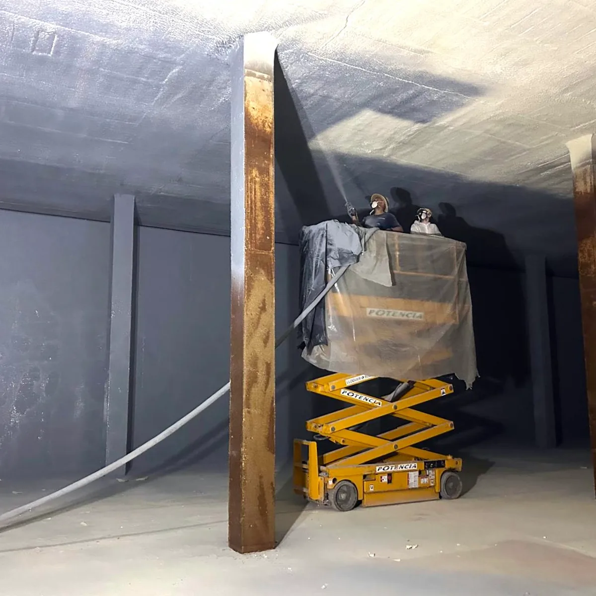 Operario sobre plataforma de tijera proyectando bajo el forjado de techo del depósito